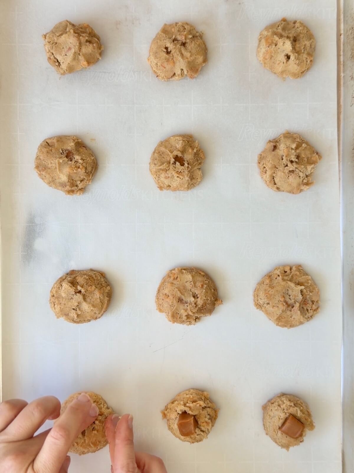 Twelve sourdough apple cookie dough balls each with a piece of caramel on a parchment-lined baking sheet.