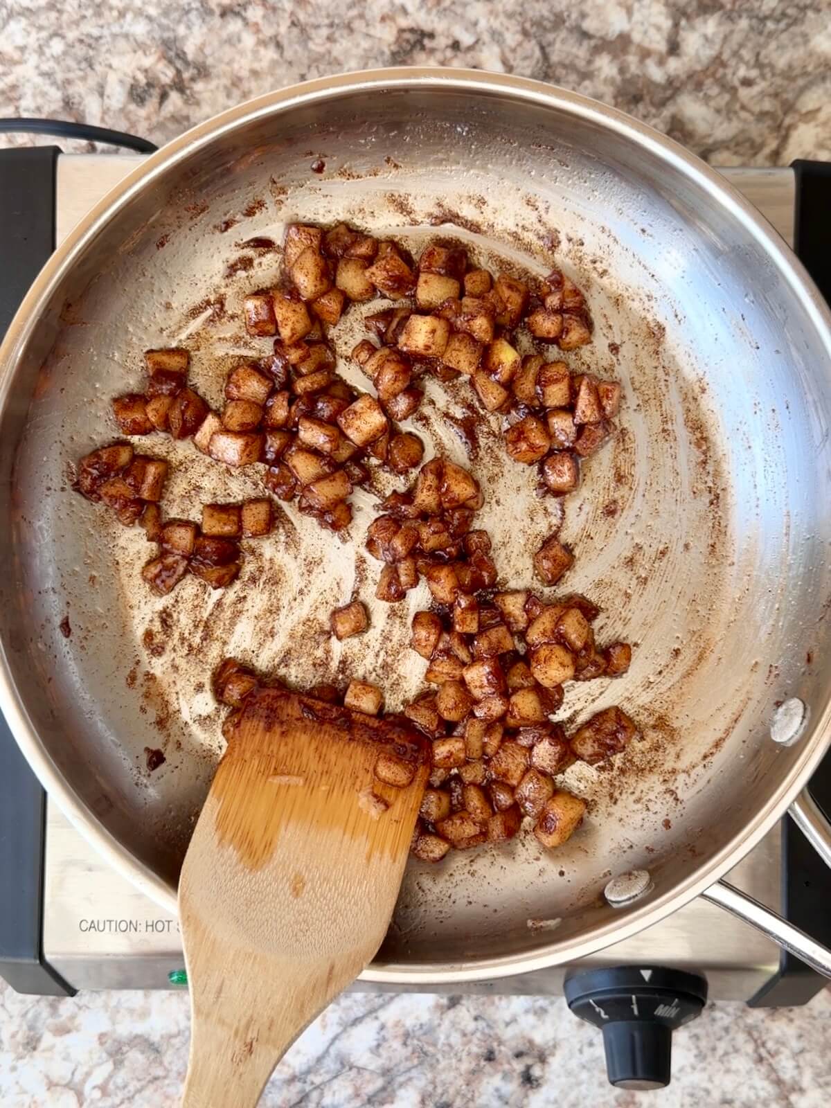 Diced apples cooking in a stainless steel skillet with brown sugar and cinnamon.