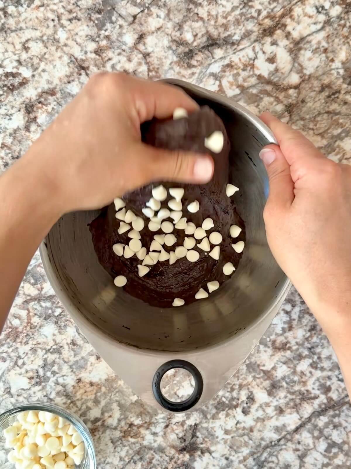 White chocolate chips being stretched and folded into the black cocoa dough.