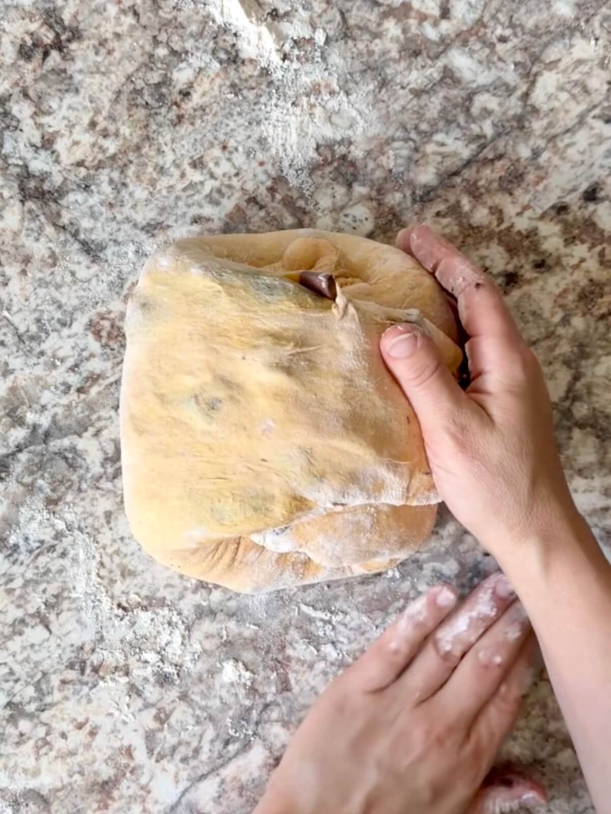 Halloween sourdough bread dough being shaped on a floured counter.