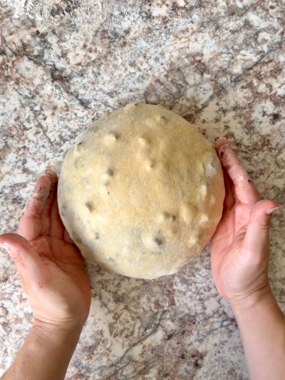Halloween sourdough bread dough being shaped into a ball on a floured counter.