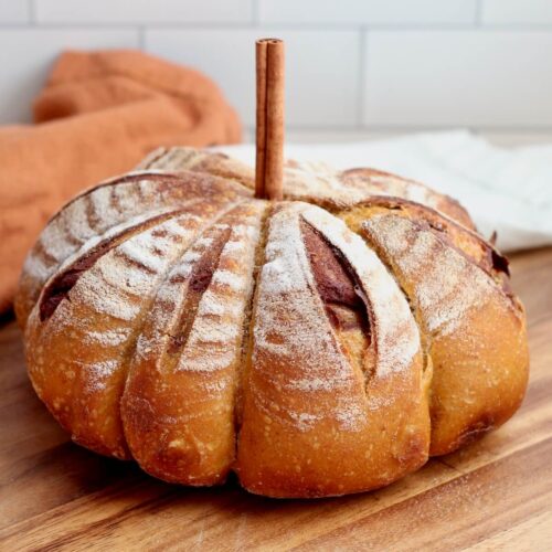 A pumpkin-shaped loaf of pumpkin spice sourdough bread with a cinnamon stick stem.