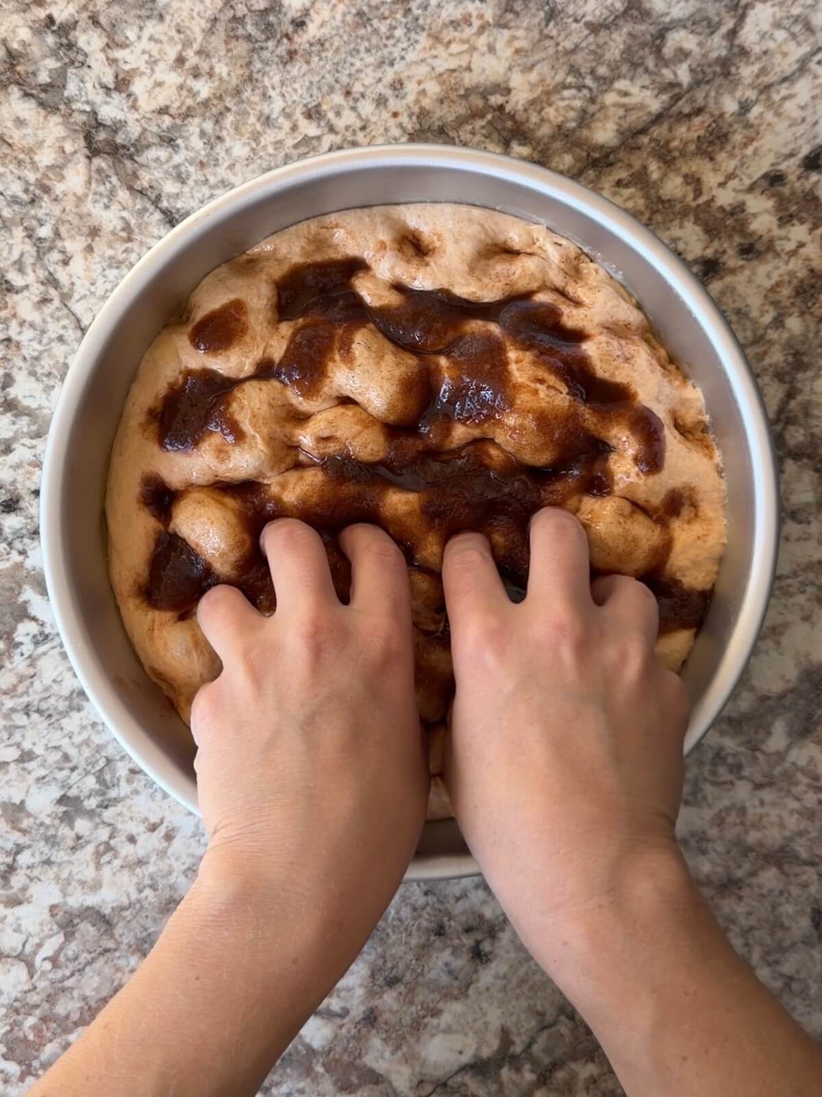 Fingers poking a mixture of butter, sugar, and pumpkin pie spice into the focaccia dough.