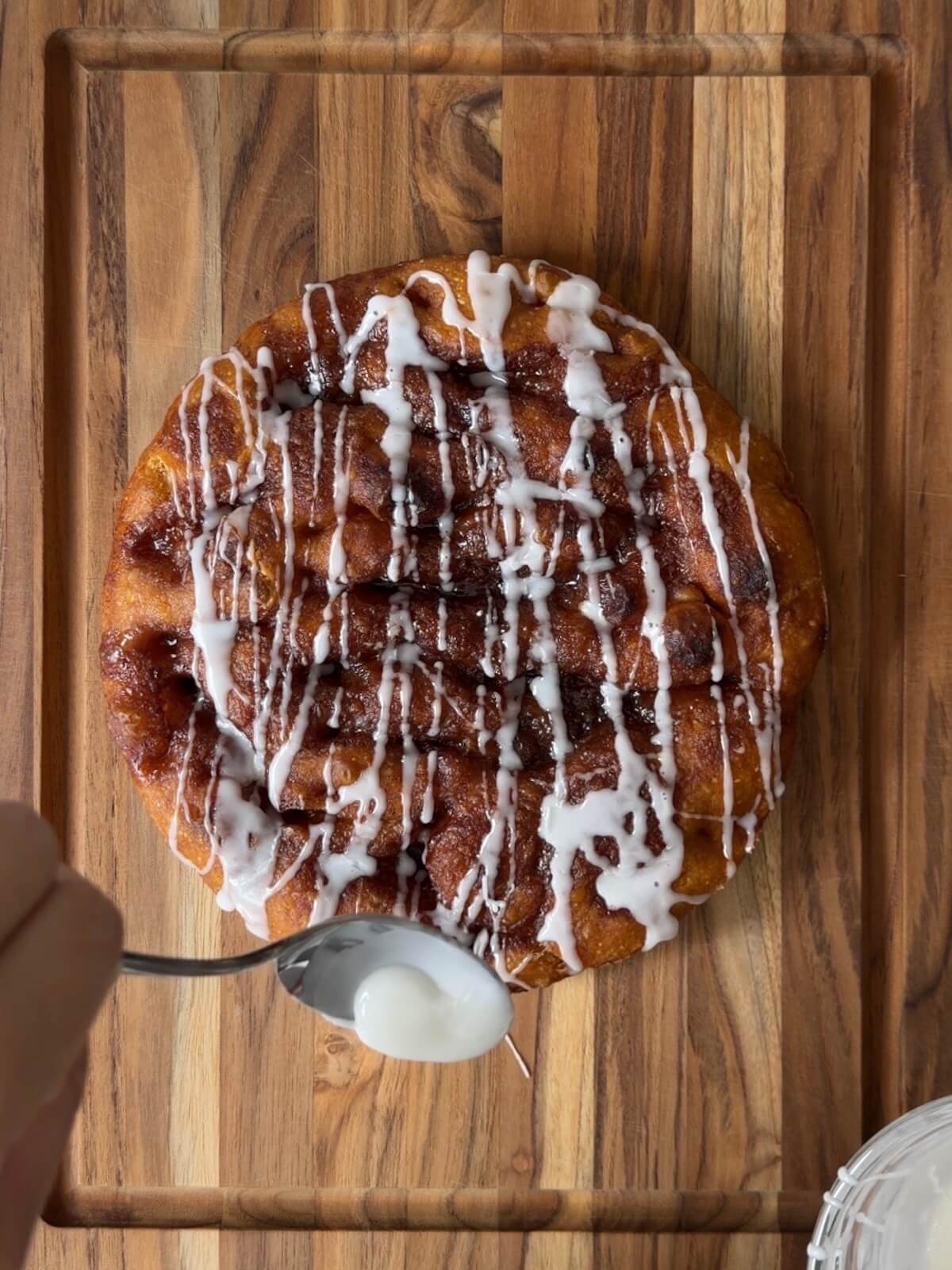 A round sweet sourdough pumpkin focaccia on a cutting board being drizzled with icing.