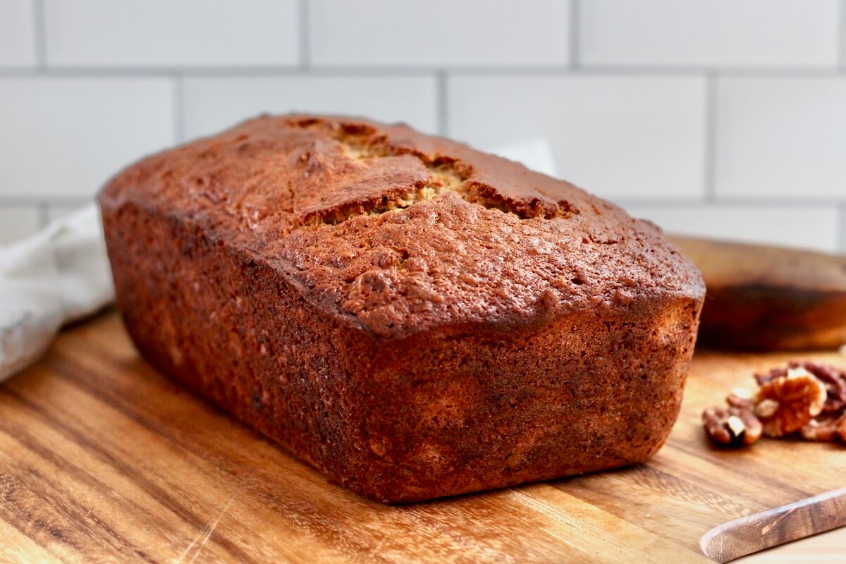 A whole loaf of sourdough discard banana bread with brown butter and toasted pecans on a wooden cutting board.