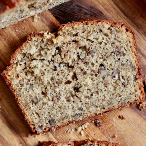 A slice of brown butter sourdough banana bread with toasted pecans on a wooden cutting board.