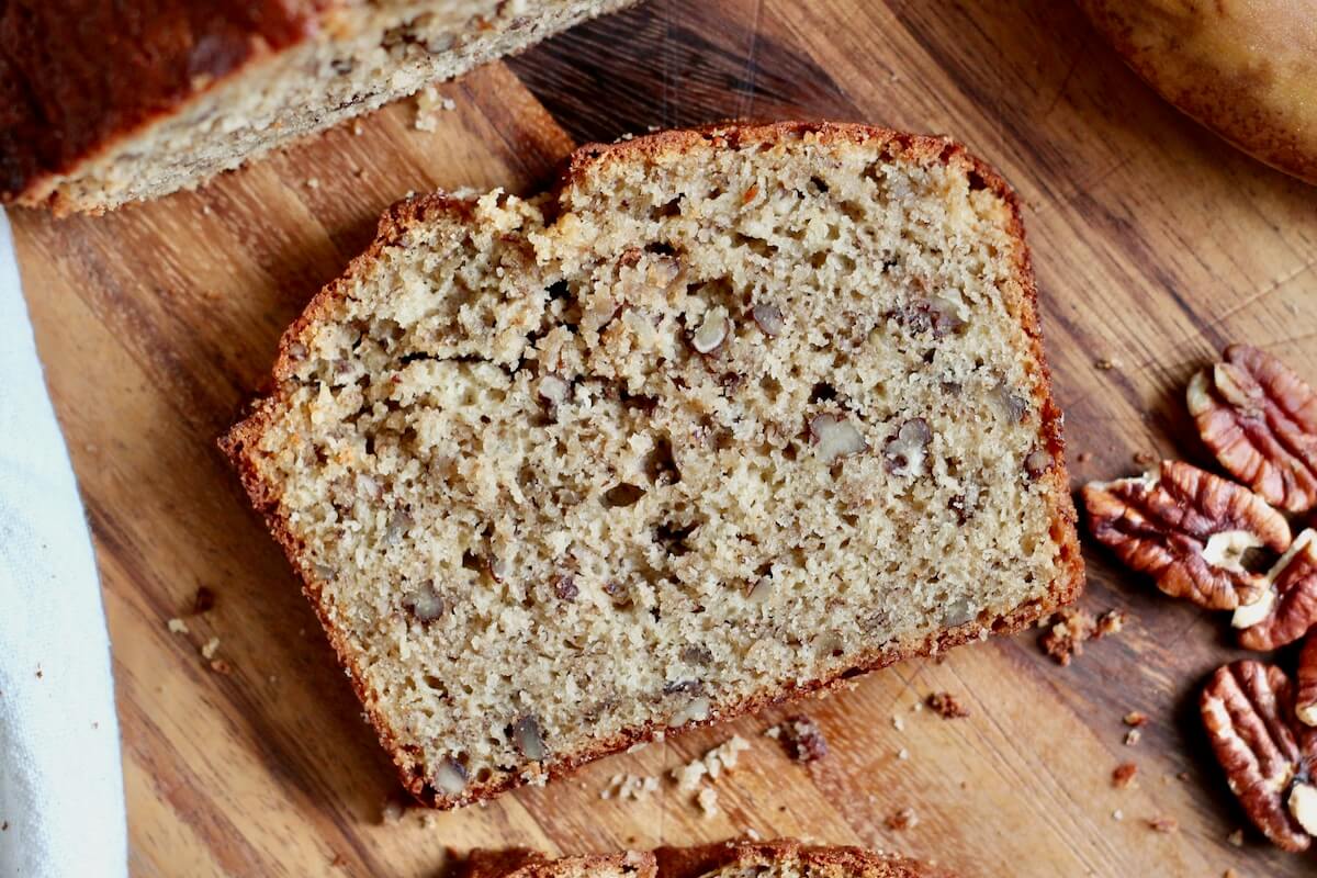 A slice of brown butter sourdough banana bread with toasted pecans on a wooden cutting board.
