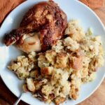 A small white plate with sourdough bread stuffing and a roasted chicken leg.