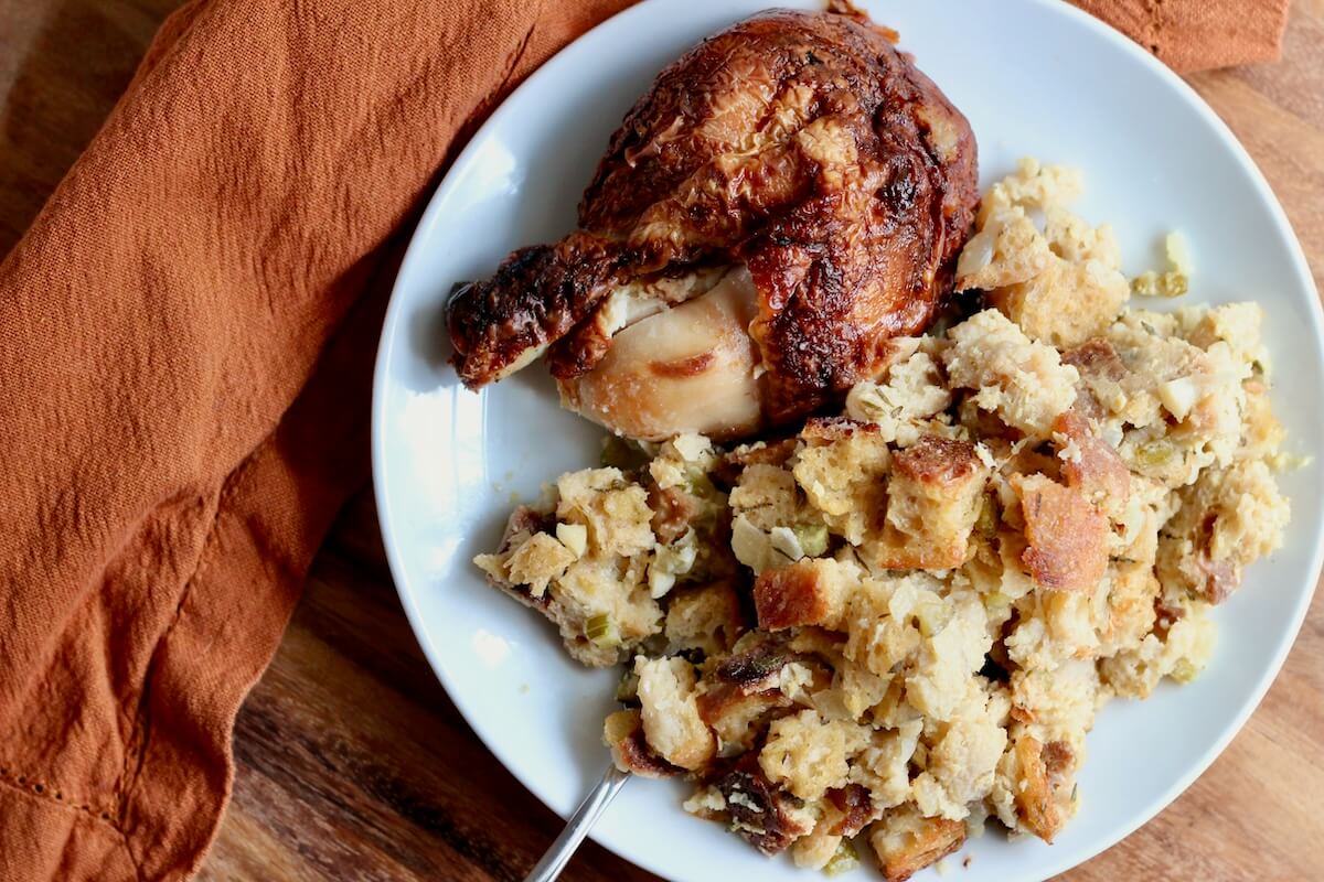 A small white plate with sourdough bread stuffing and a roasted chicken leg.