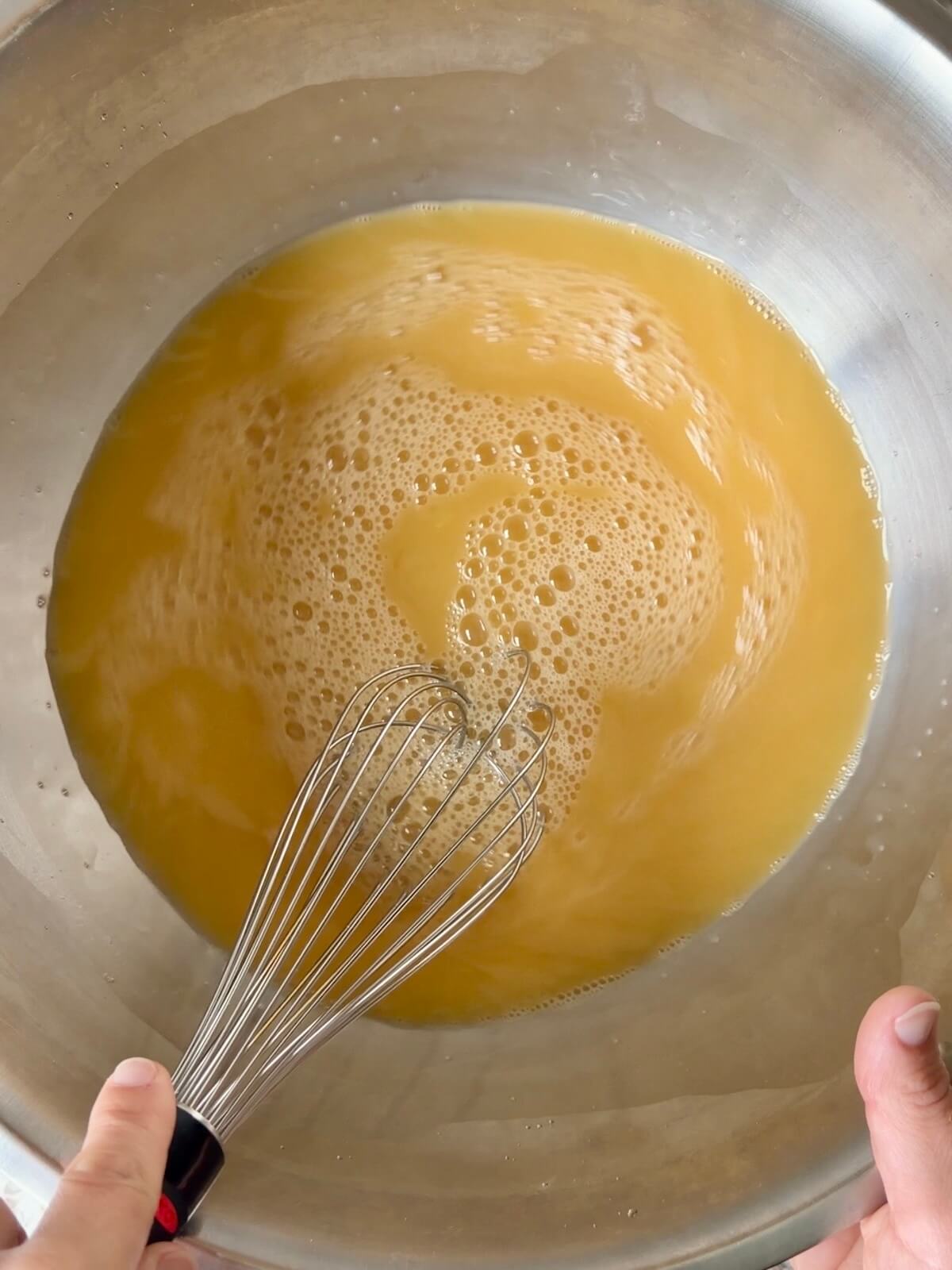 Chicken stock and eggs being whisked together in a large bowl.
