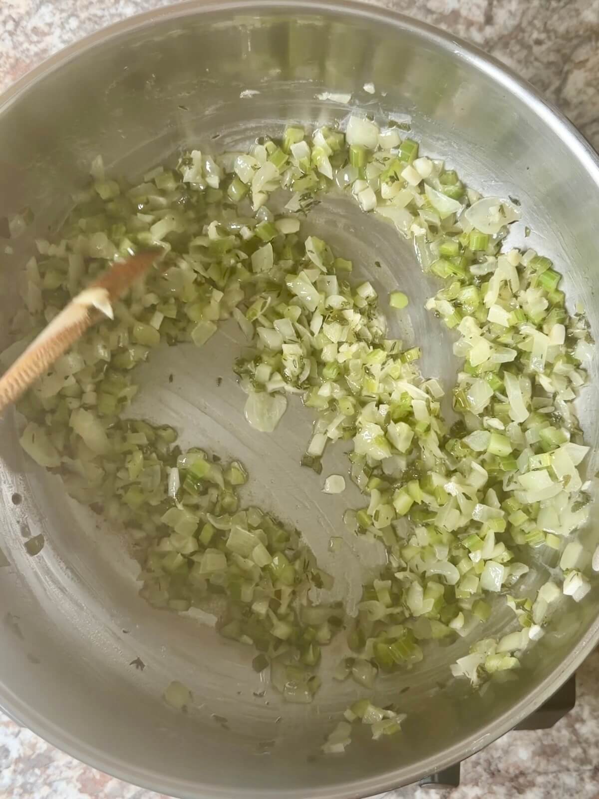 Celery, onion, garlic, sage, and thyme being sautéed in a stainless steel skillet.