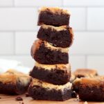 A stack of five sourdough cheesecake brownies with more brownies scattered around the stack.