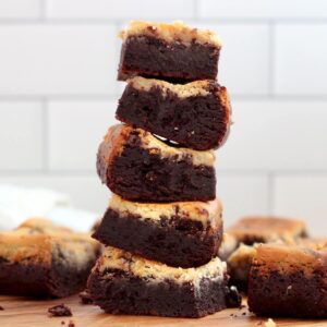 A stack of five sourdough cheesecake brownies with more brownies scattered around the stack.