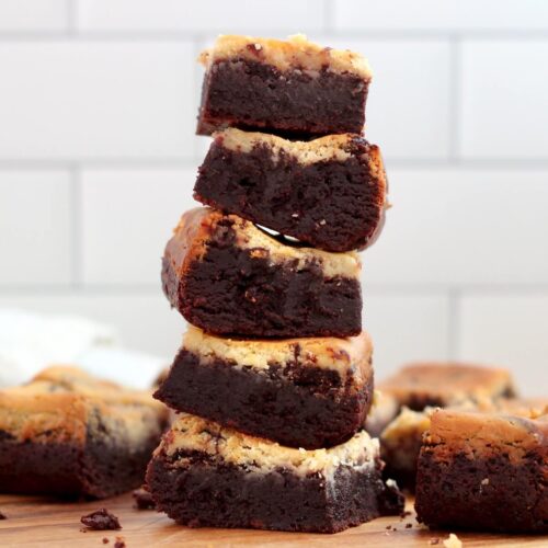 A stack of five sourdough cheesecake brownies with more brownies scattered around the stack.