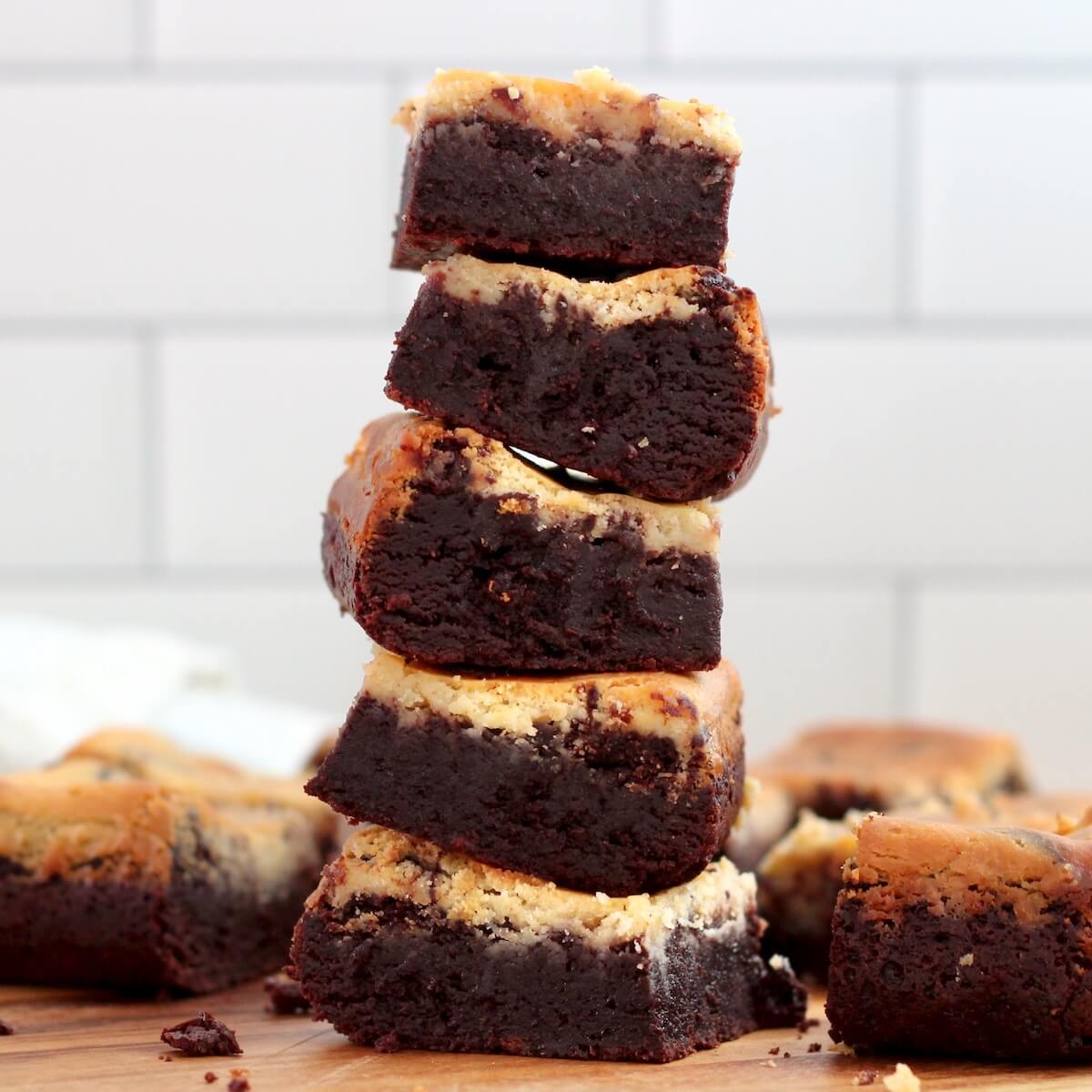 A stack of five sourdough cheesecake brownies with more brownies scattered around the stack.