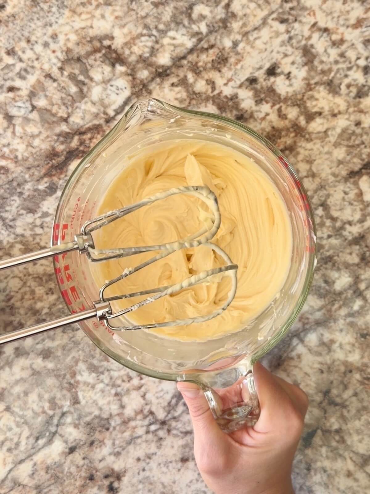The cheesecake layer mixed together with a hand mixer in a glass measuring cup.