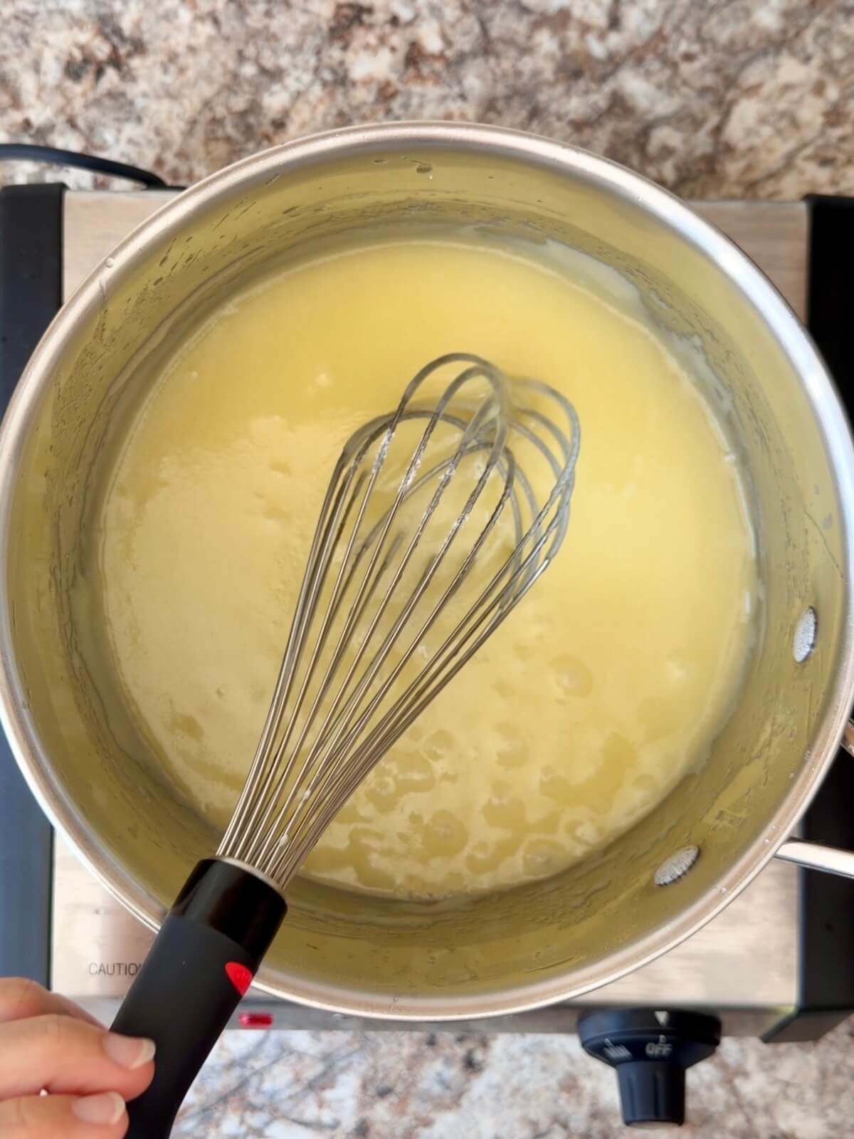 Butter and sugar being cooked together in a stainless steel pot.