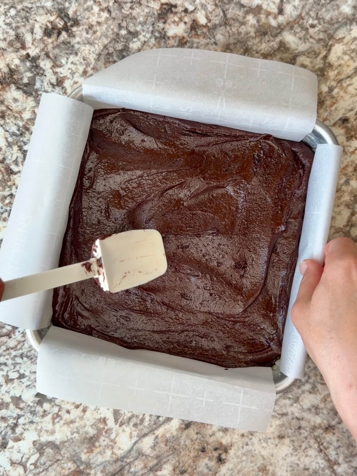 Sourdough brownie batter spread into a parchment-lined square baking pan.