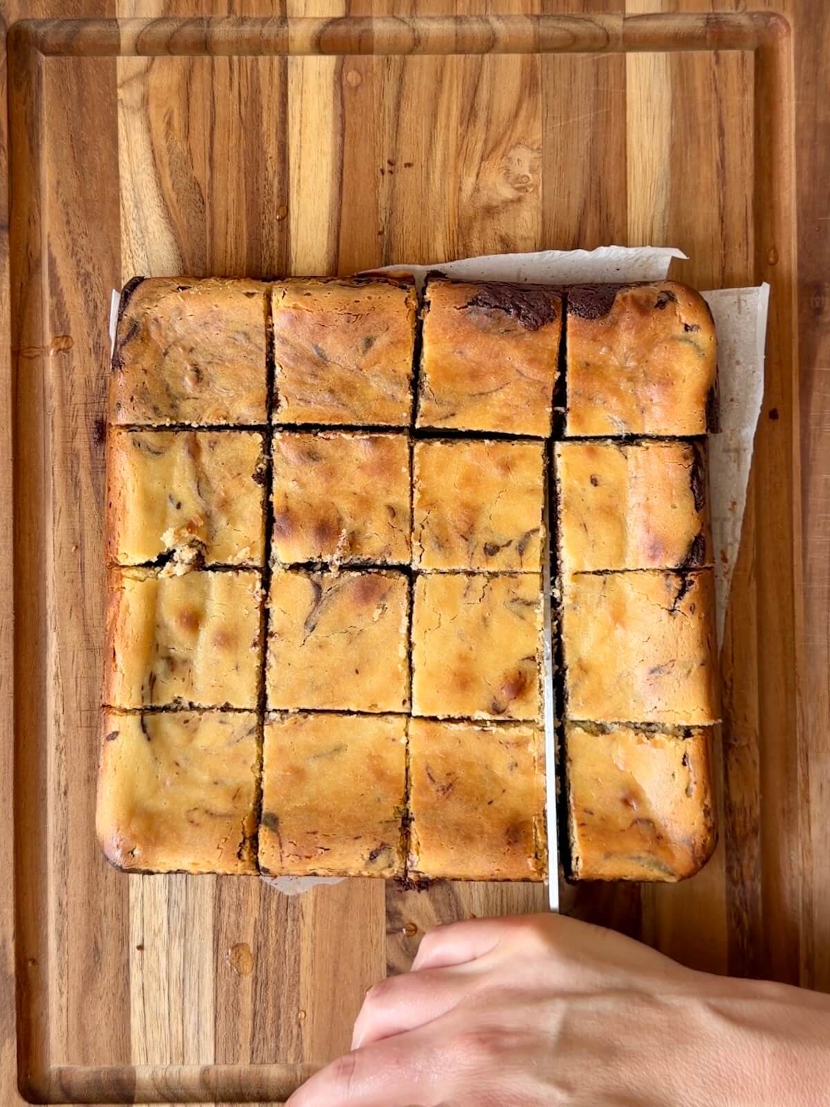 The sourdough cheesecake brownies being cut into 16 squares on a wooden cutting board.