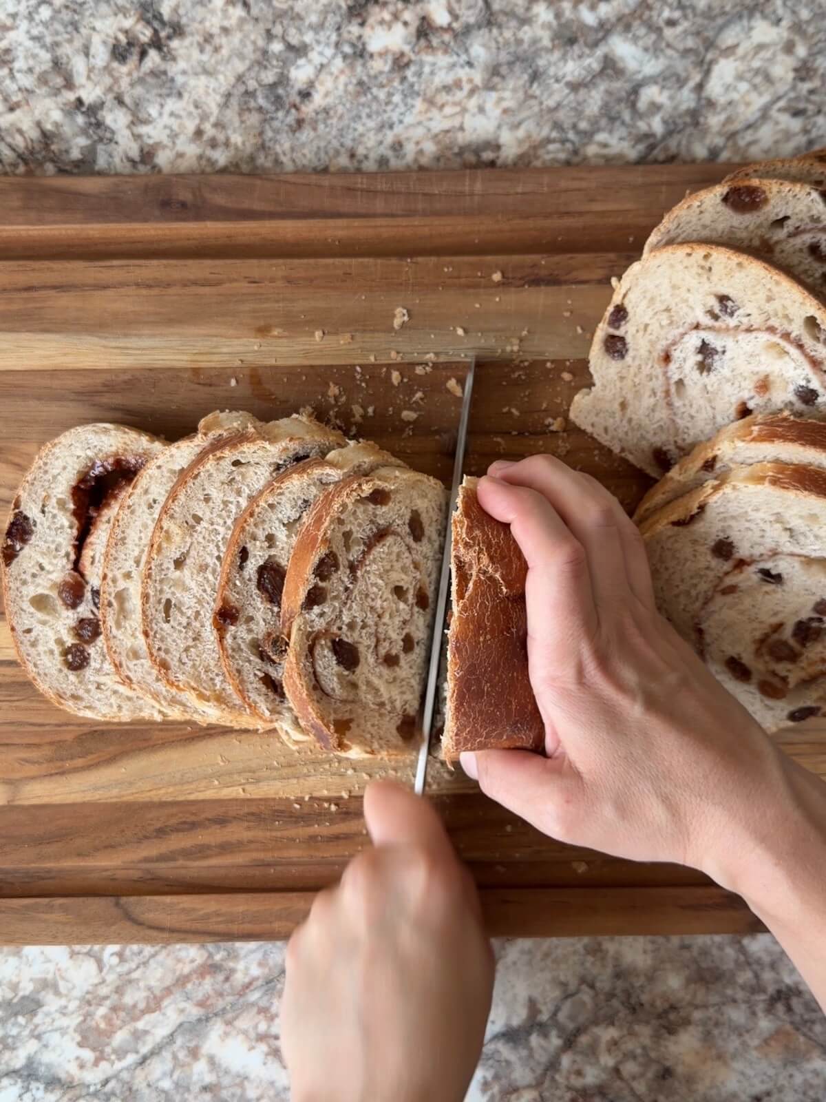 A loaf of sourdough cinnamon raisin bread being sliced on a wooden cutting board.