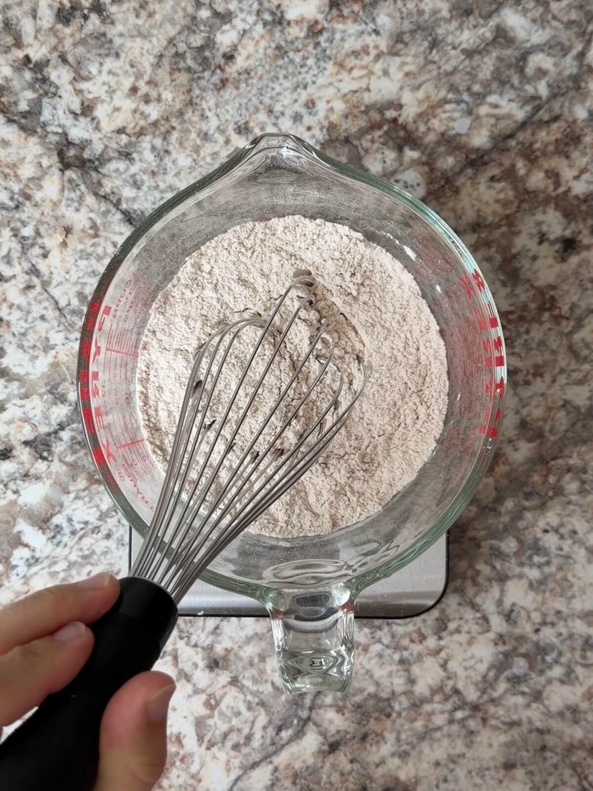 Flour, pumpkin pie spice, and other dry ingredients being whisked together in a large glass measuring cup.