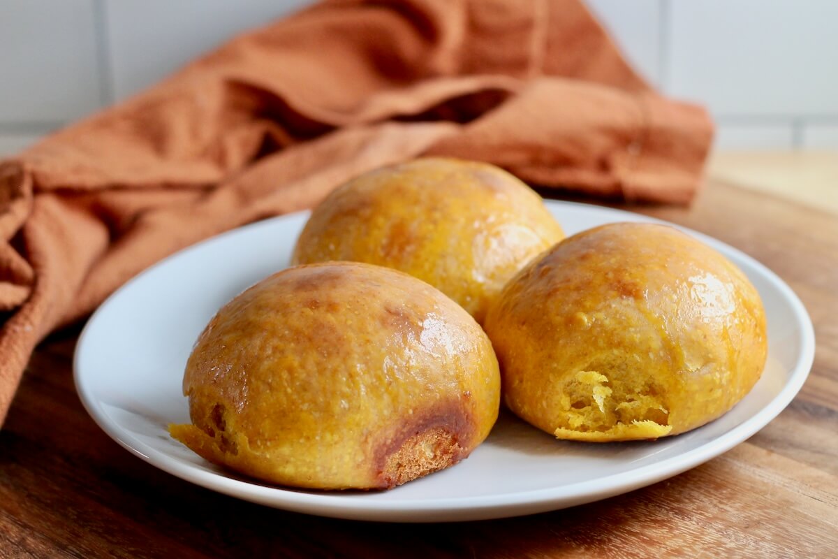 Three pumpkin sourdough dinner rolls on a small white plate.