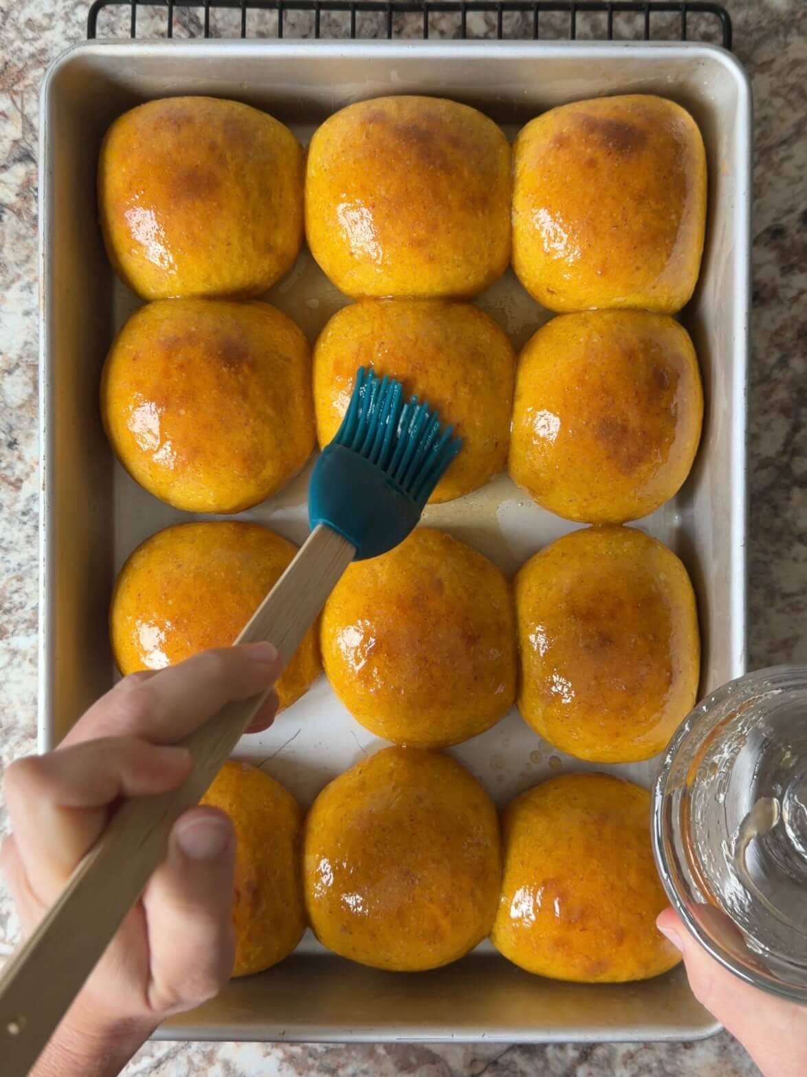 The sourdough pumpkin dinner rolls being brushed with salted maple butter in a baking pan.