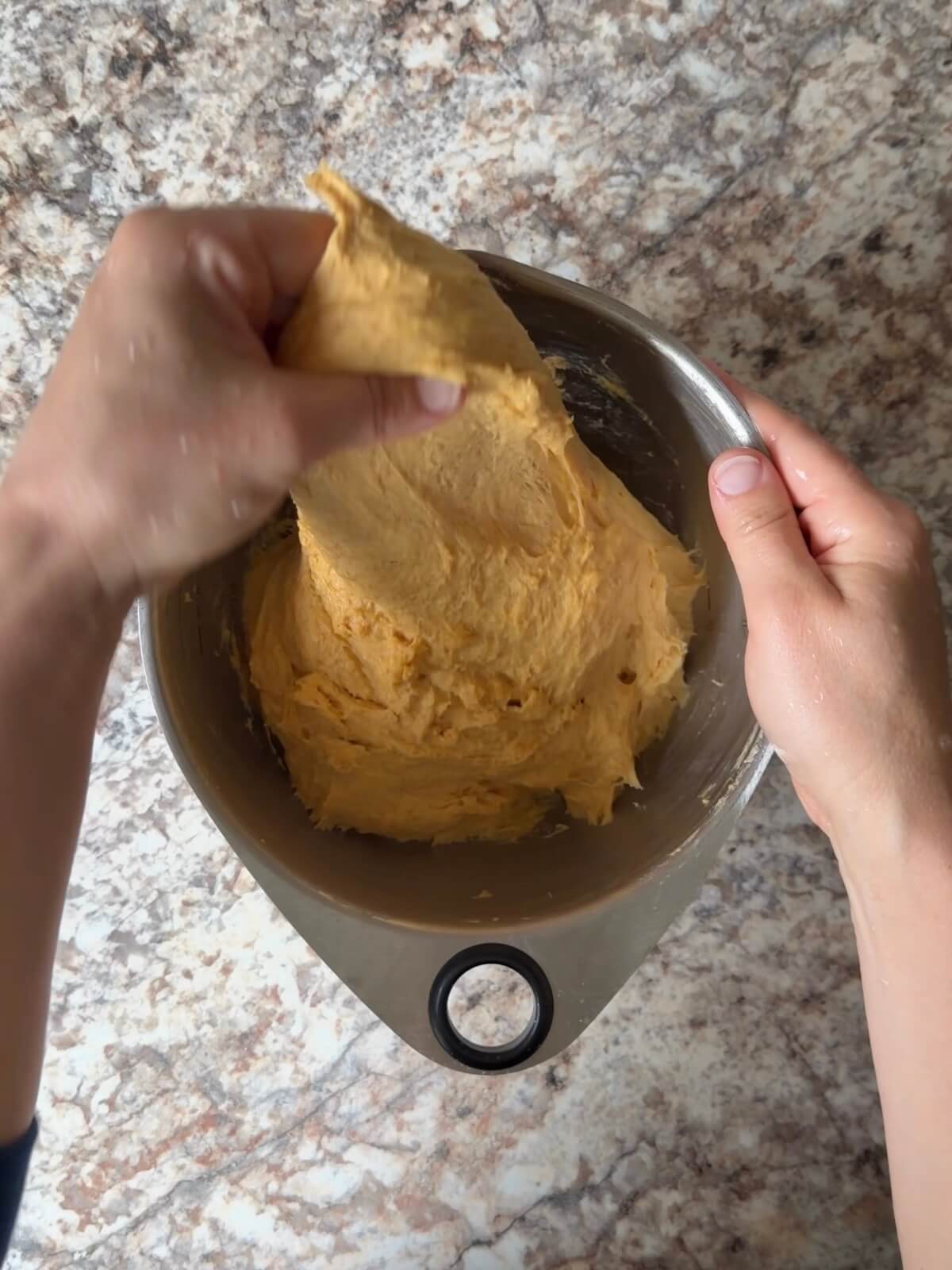 Sourdough pumpkin dinner roll dough being stretched and folded in a mixing bowl.