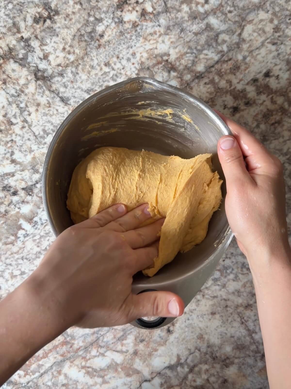 Sourdough pumpkin dinner roll dough being stretched and folded in a mixing bowl.
