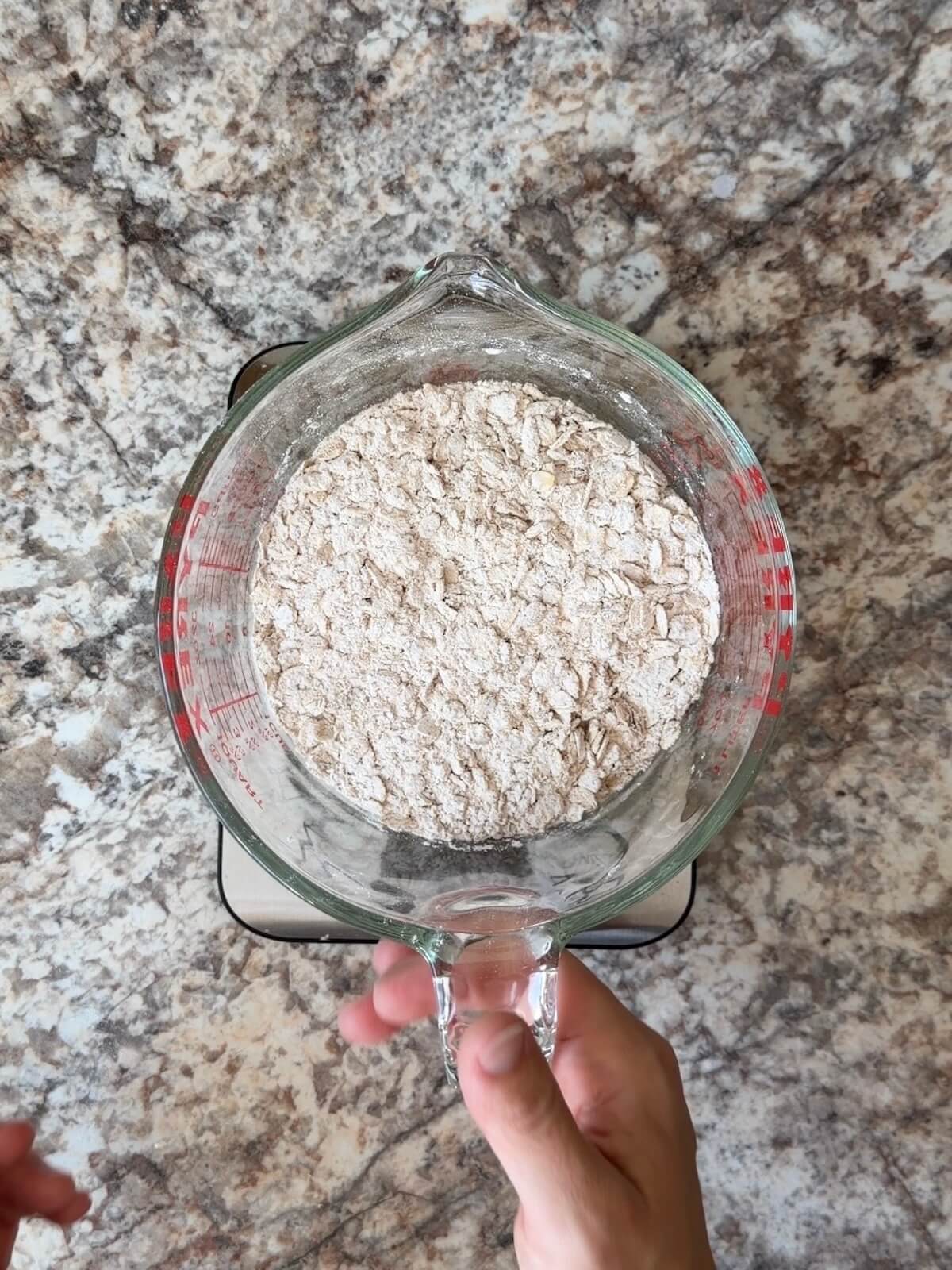 Rolled oats, pumpkin spice, and other dry ingredients whisked together in a large glass measuring cup.