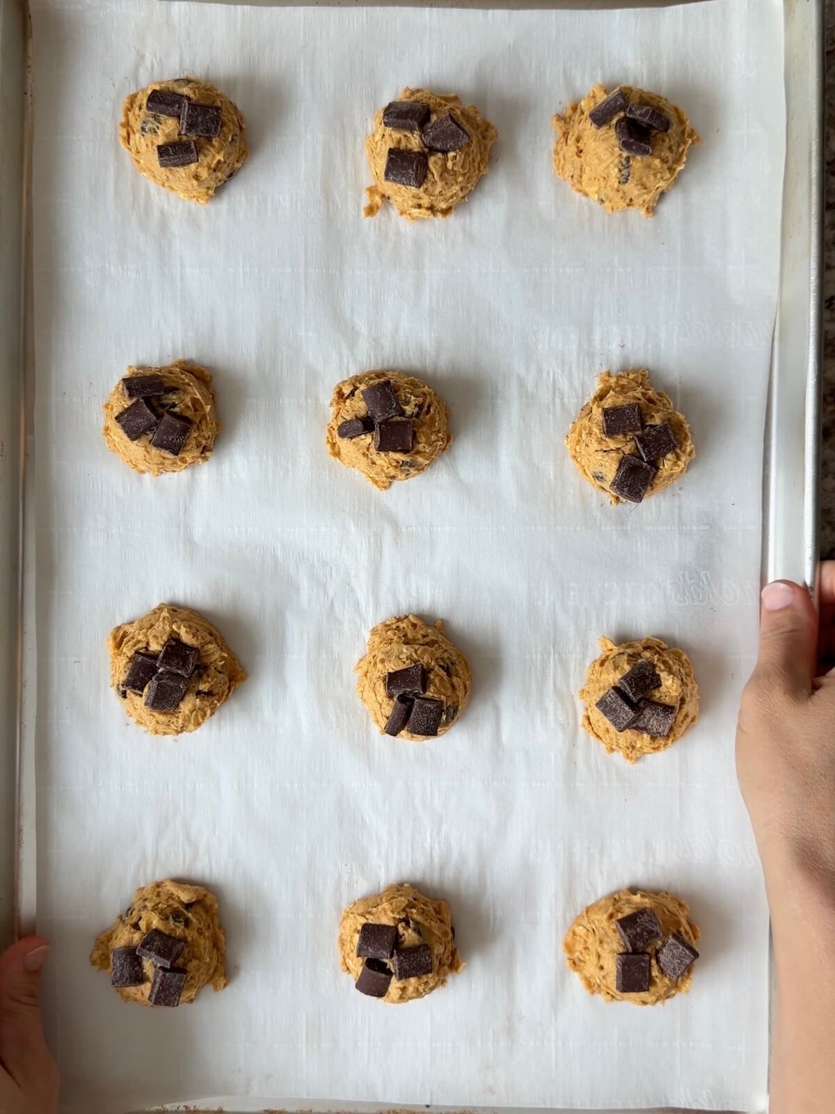 Twelve tablespoon-sized cookie dough balls on a baking sheet with chocolate chunks pressed on top.