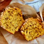 A sourdough pumpkin muffin split in half on a piece of parchment paper.