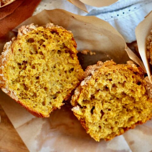 A sourdough pumpkin muffin split in half on a piece of parchment paper.