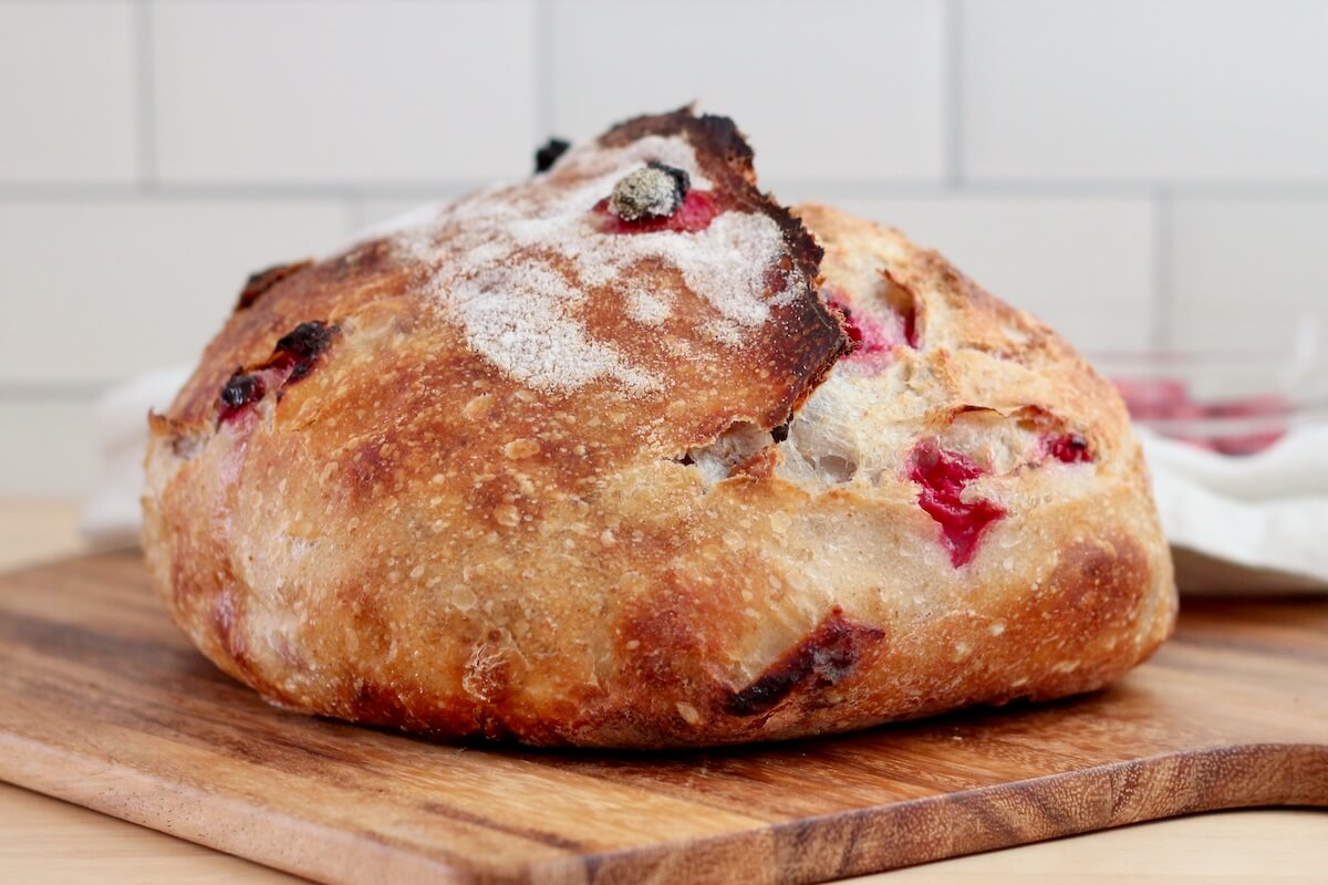 A whole loaf of cranberry walnut sourdough bread on a wooden cutting board.
