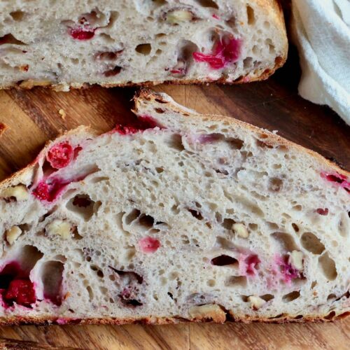 A slice of cranberry walnut sourdough bread on a wooden cutting board.