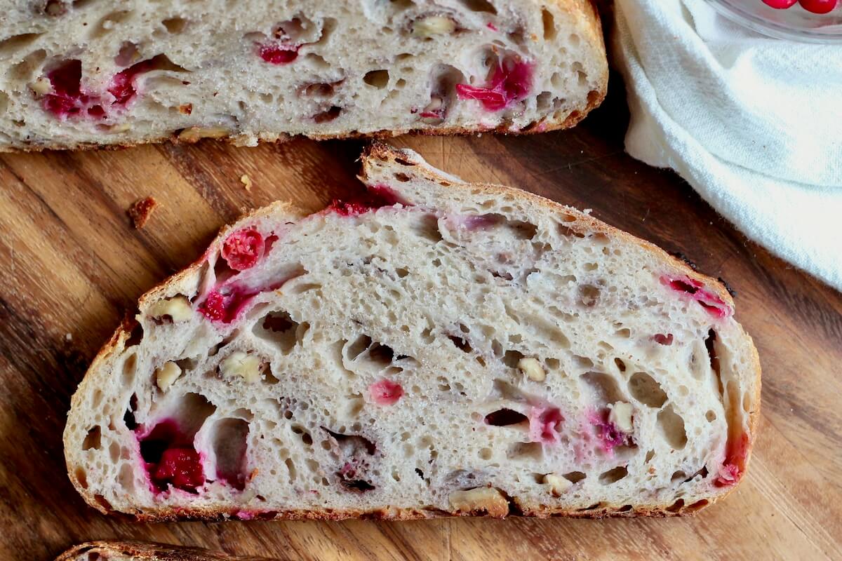 A slice of cranberry walnut sourdough bread on a wooden cutting board.
