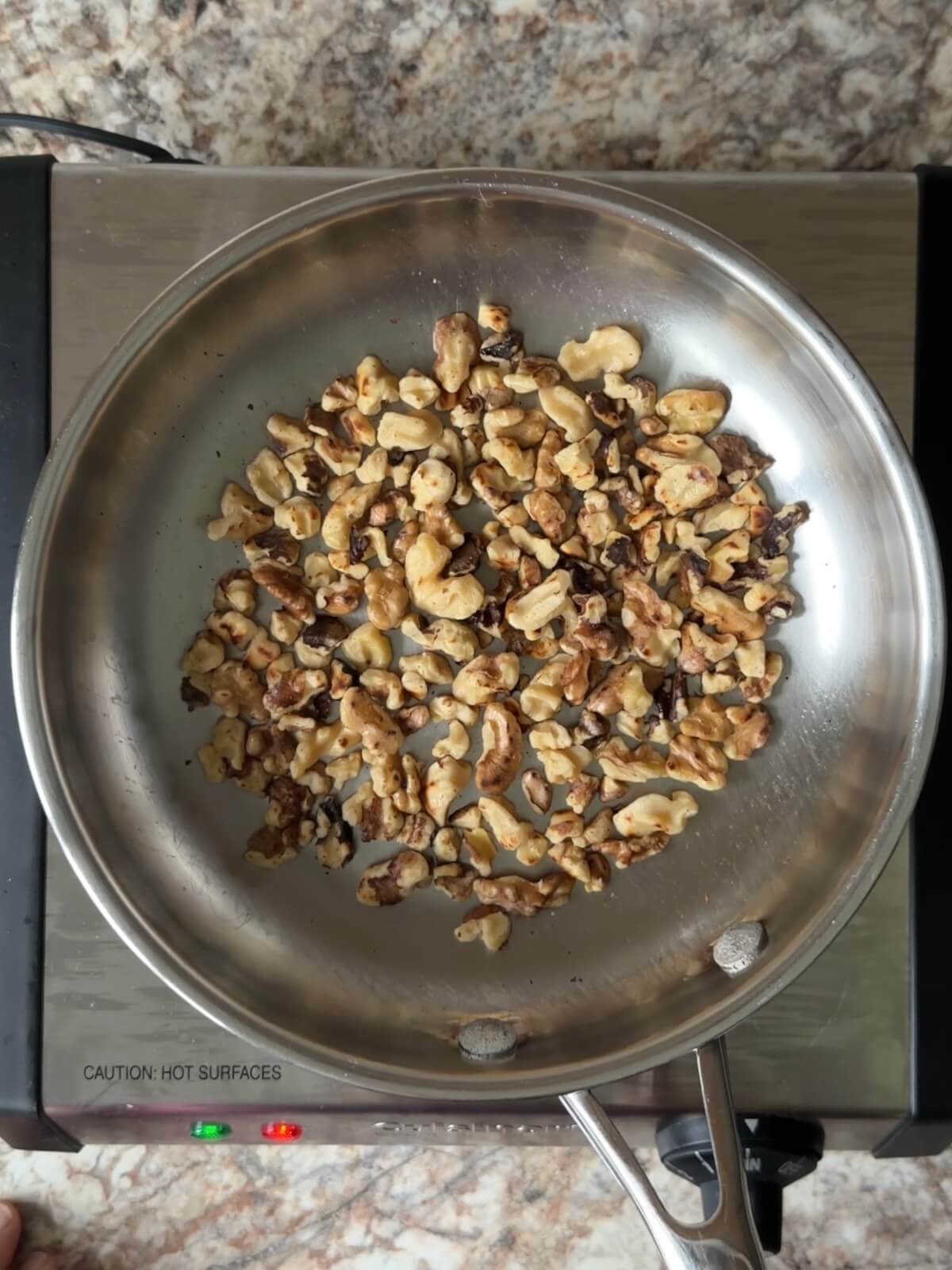 Chopped walnuts toasting in a stainless steel skillet.