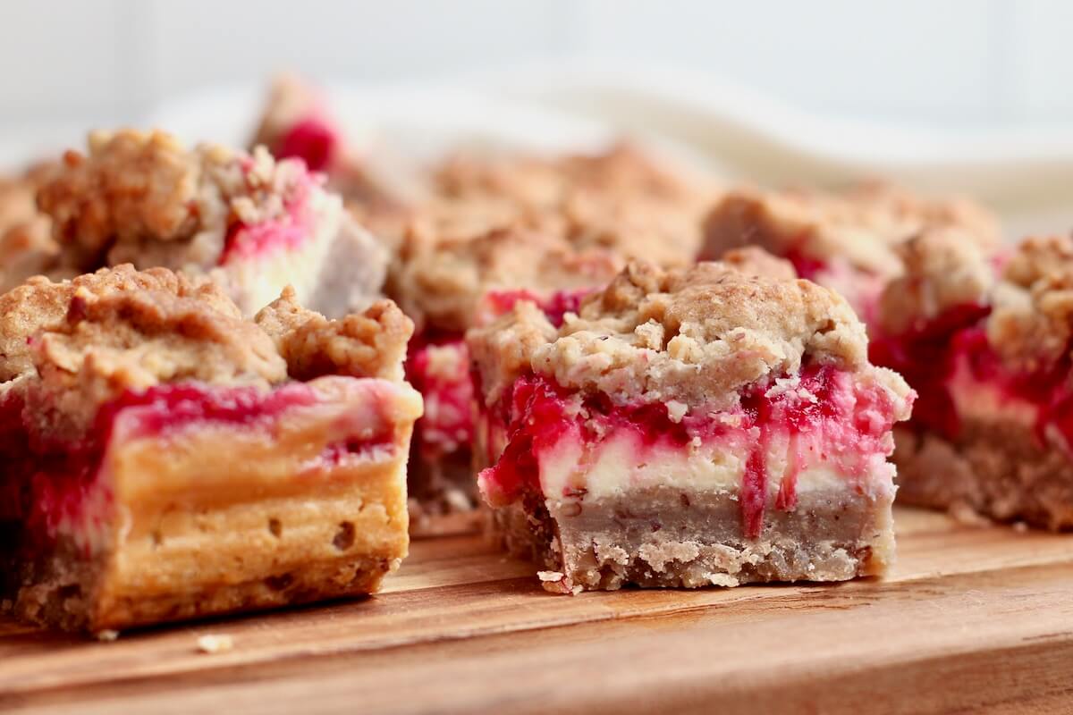 Several sourdough cranberry cheesecake bars on a wooden cutting board.