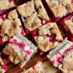 Squares of sourdough cranberry cheesecake bars on a wooden cutting board.