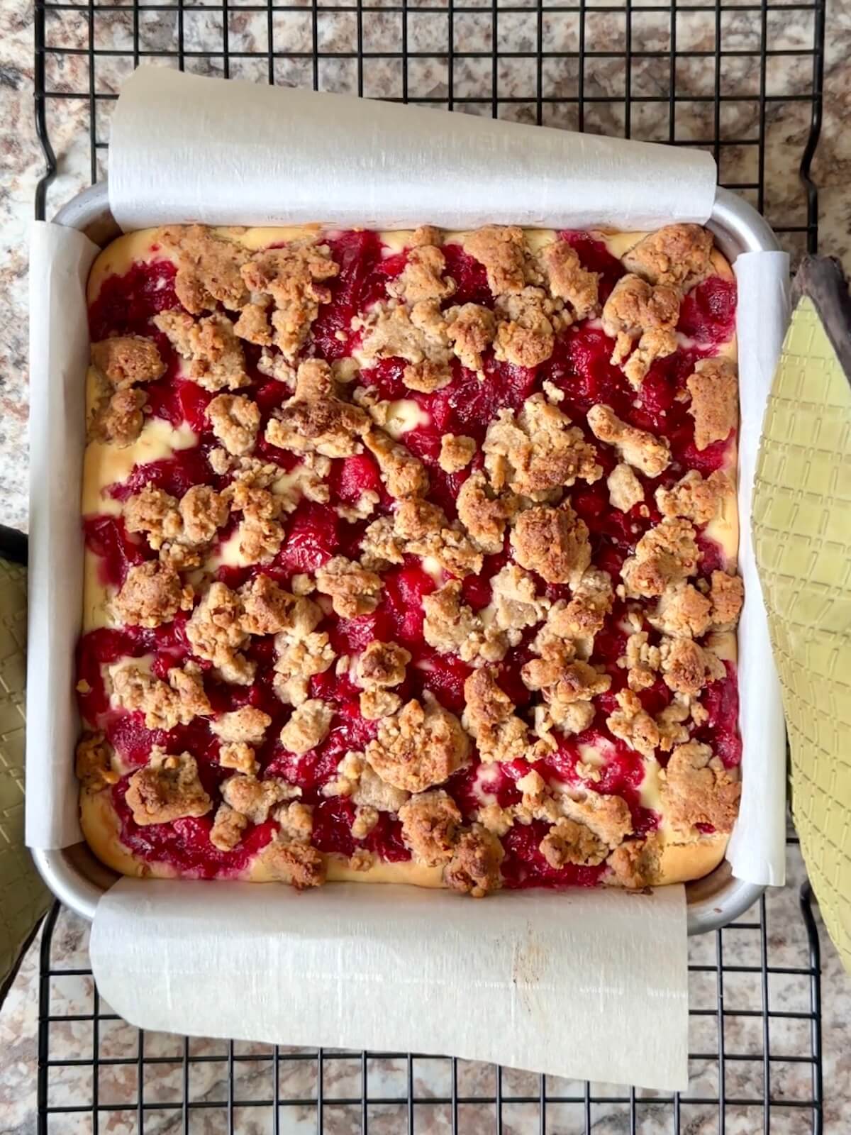 Baked sourdough cranberry cheesecake bars in a square, parchment-lined baking pan.