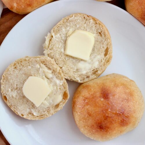 Two sourdough dinner rolls on a plate. One is whole and the other is cut in half and buttered.