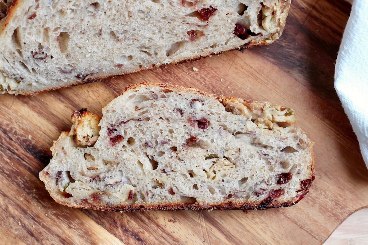 A slice of Thanksgiving stuffing sourdough bread on a wooden cutting board.