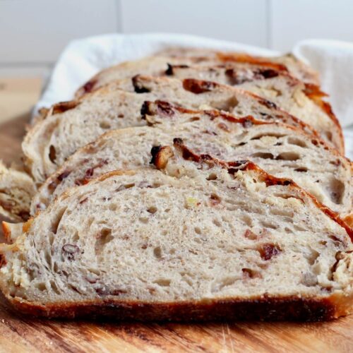 A sliced loaf of Thanksgiving stuffing sourdough bread on a wooden cutting board.