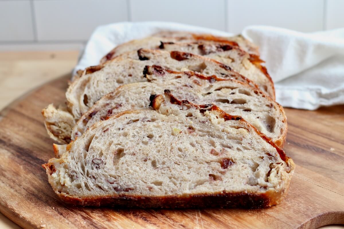 A sliced loaf of Thanksgiving stuffing sourdough bread on a wooden cutting board.
