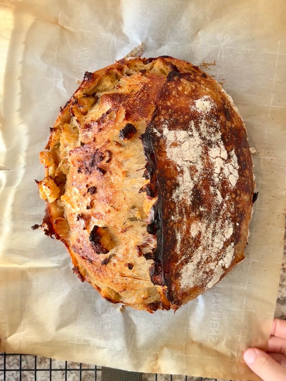 A baked loaf of Thanksgiving stuffing sourdough bread on a wire cooling rack.