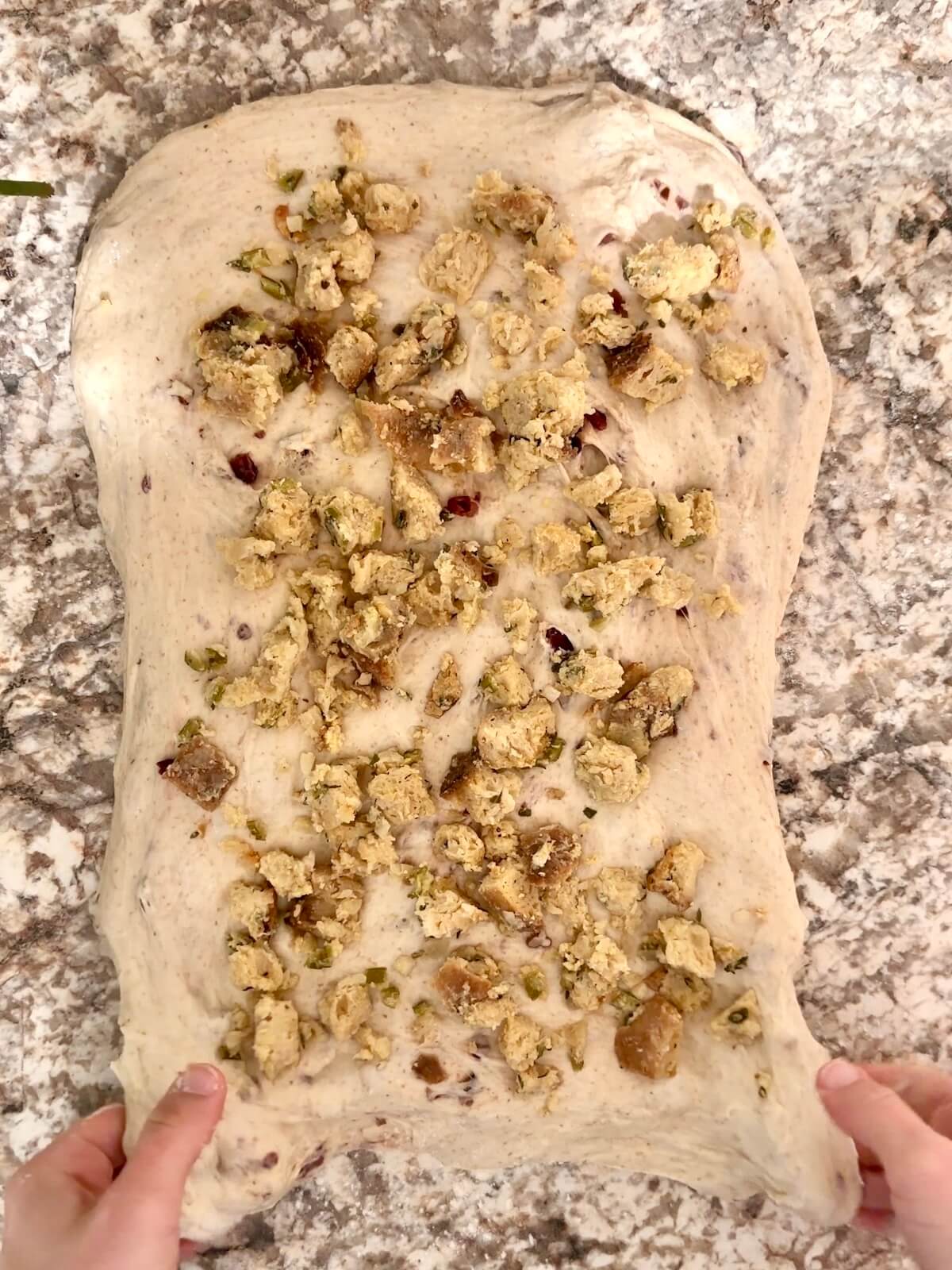 Thanksgiving stuffing spread on top of sourdough bread dough that's been stretched into a rectangle on a floured counter.
