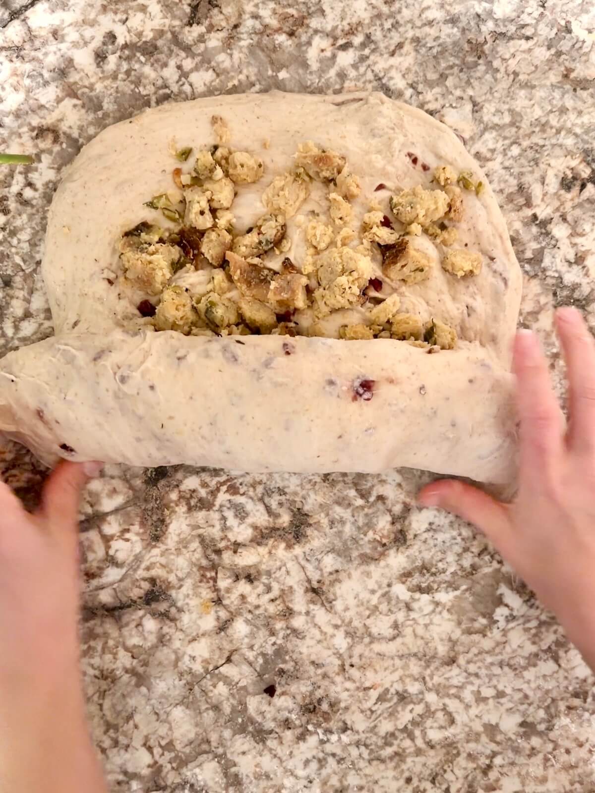 Stuffing being rolled into sourdough bread dough on a floured counter.